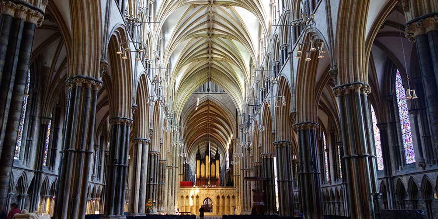 Panoramic interior image of nave of Lincoln Cathedral showing columns and soaring, arched ceiling