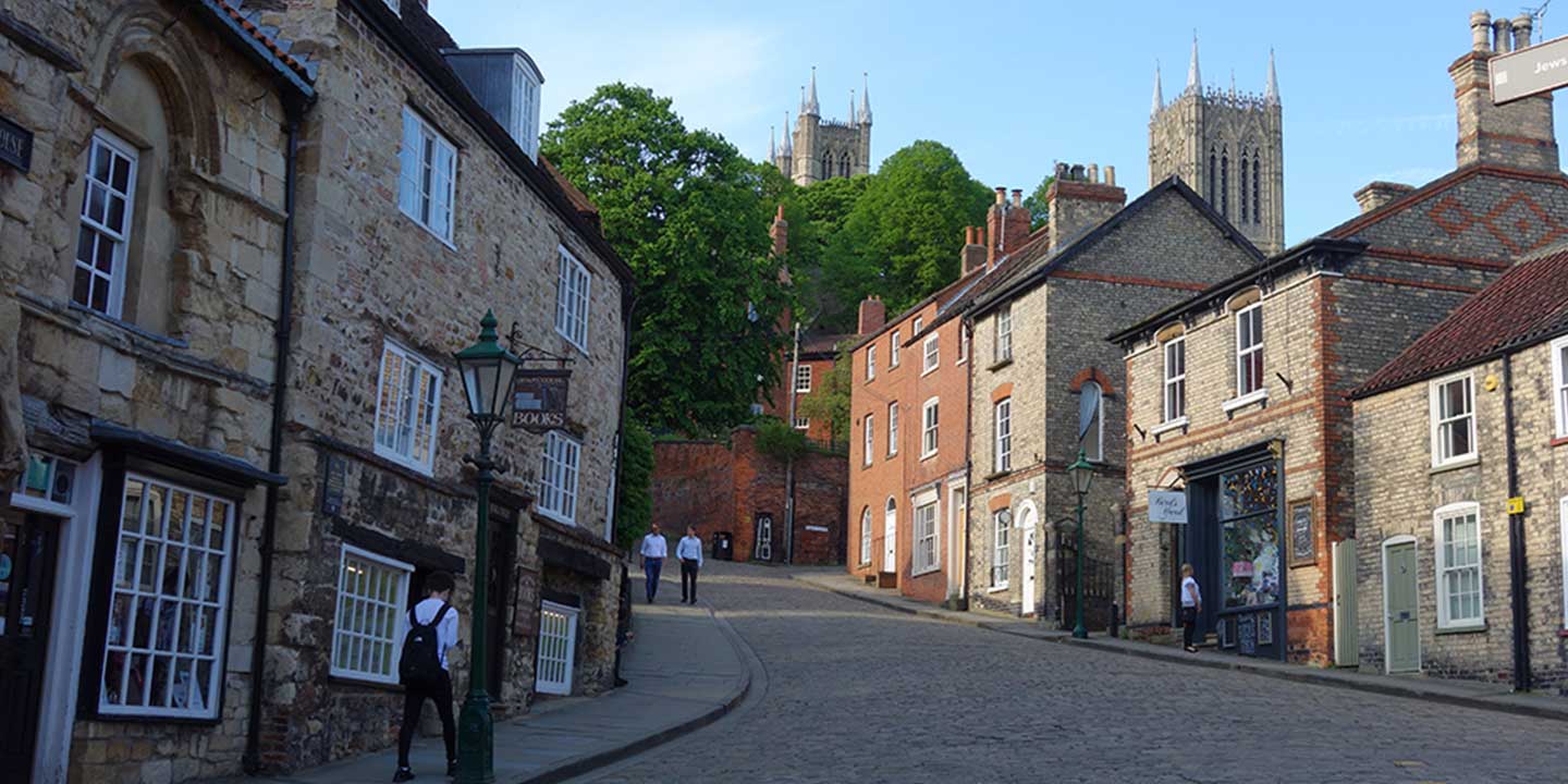 Panoramic image of Steep Hill, Lincoln, England, with cobbled streets, shops and restaurants with spire of Lincoln Cathedral in distance