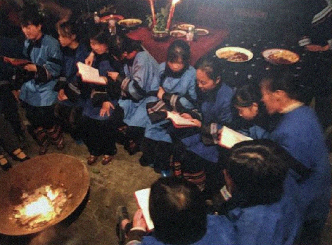 Photograph of women learning Nüshu in a village hall sat around a fire