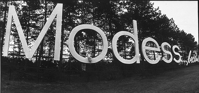 a black and white photo of large Modess...because signage with trees in the background image